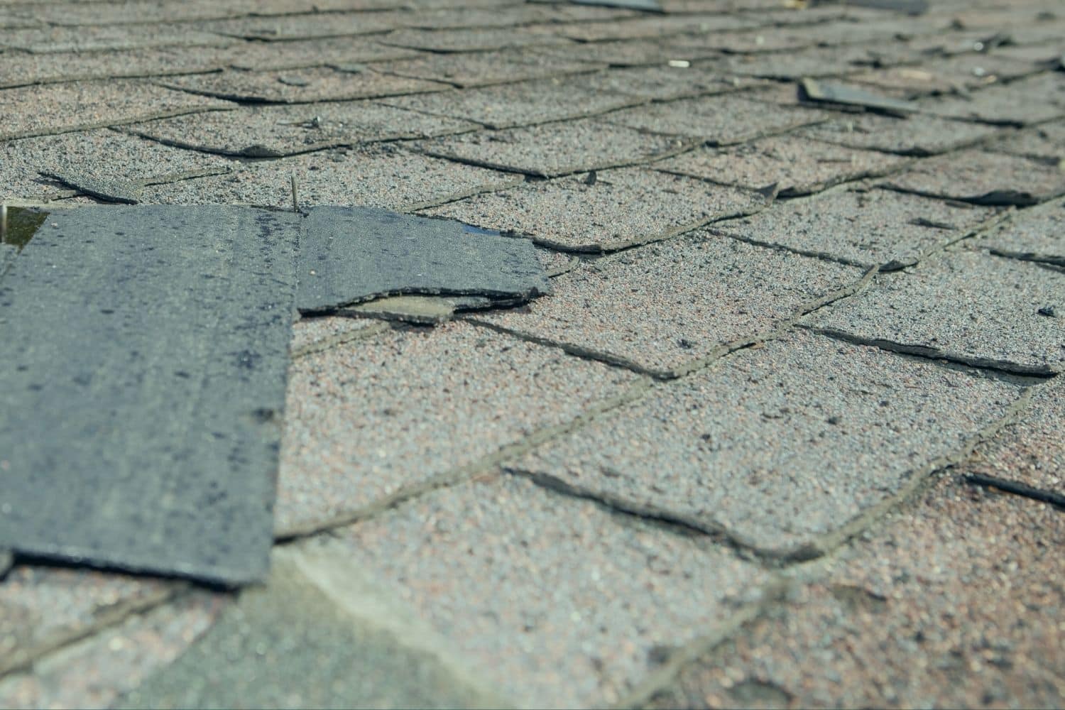 Lifted and mismatched shingles patched into an aging asphalt roof