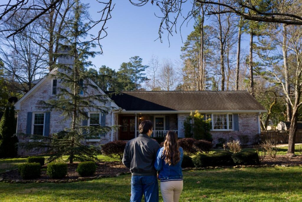 A couple standing outside in front of a suburban residential house while consulting with a home inspector during a property inspection.